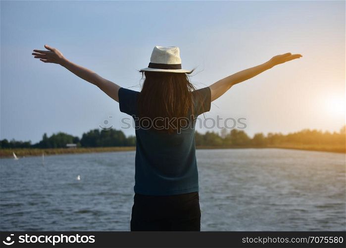 The woman wore a white T-shirt and a hat, standing on the river and the two hands on the sky.