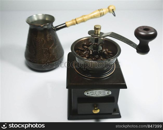 The wooden coffee grinder with coffee beans and cezva on white background