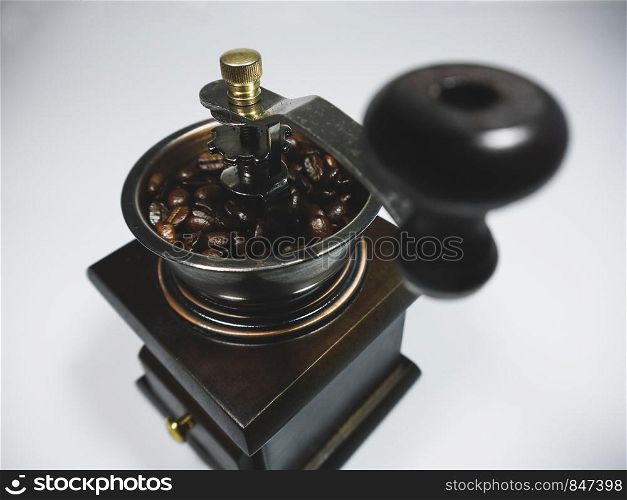 The wooden coffee grinder with coffee beans on white background. The focus on the handle