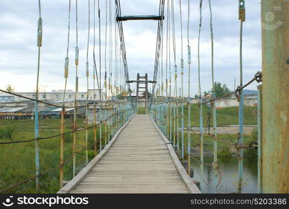 The wooden hinged bridge through the small river.