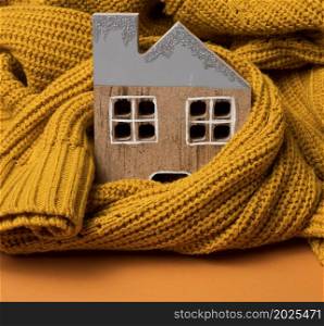 the wooden model of the house is wrapped in a warm knitted sweater. Loan concept for house insulation, alternative energy
