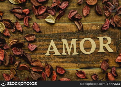 "The word "Amor" on a rustic wooden with dry red petals around"