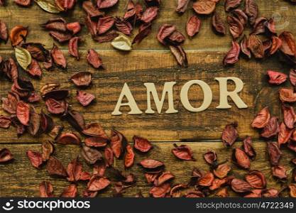 "The word "Amor" on a rustic wooden with dry red petals around"
