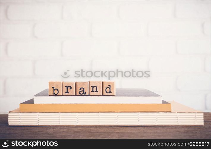 The word Brand, text on wooden cubes on top books. Background space, vintage minimal. Name, term, design, symbol, feature of organization products. Business customer, marketing, advertising Concepts.
