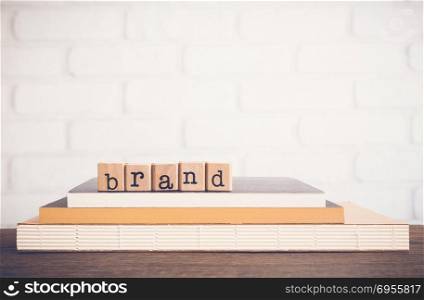 The word Brand, text on wooden cubes on top books. Background space, vintage minimal. Name, term, design, symbol, feature of organization products. Business customer, marketing, advertising Concepts.