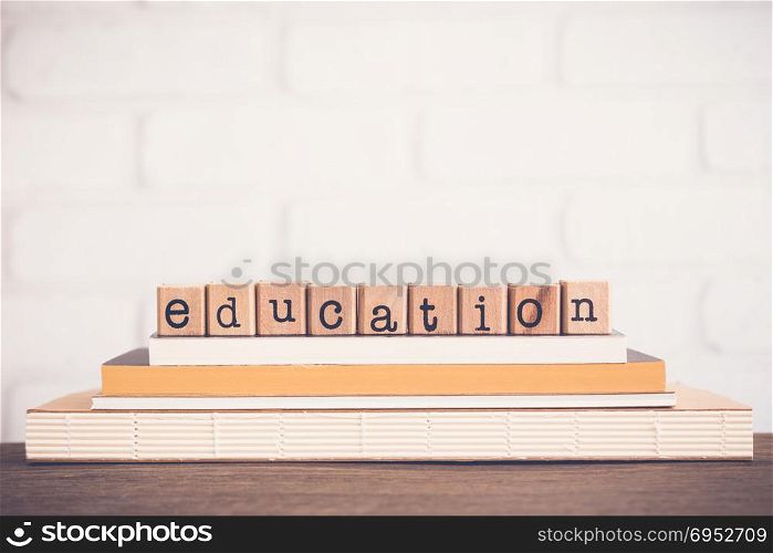 The word Education, alphabet on wooden rubber stamps on top of books and table. White bricks background, blank copy space, vintage and minimal style. School learning course, academic curriculum.