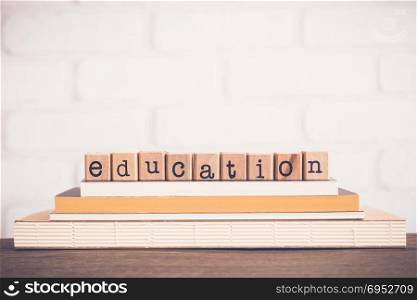 The word Education, alphabet on wooden rubber stamps on top of books and table. White bricks background, blank copy space, vintage and minimal style. School learning course, academic curriculum.