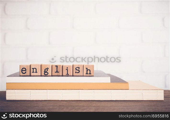 The word English, text on wooden cubes on top of books. Background copy space, vintage minimal style. Concepts of language learning, course training or business of education .