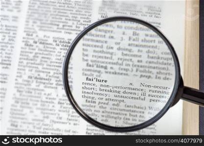 The word Failure seen through a magnifying glass in a dictionary with surrounding text blurred
