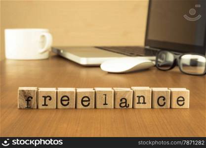 The word freelance on wood stamp stacking on desk with laptop, glasses and a cup of coffee at home office, vintage retro image style