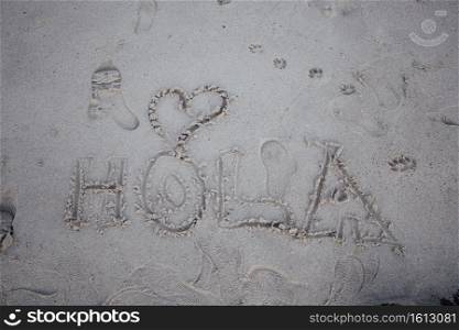 The word hi written in spanish in the sand of the beach with a heart, hola