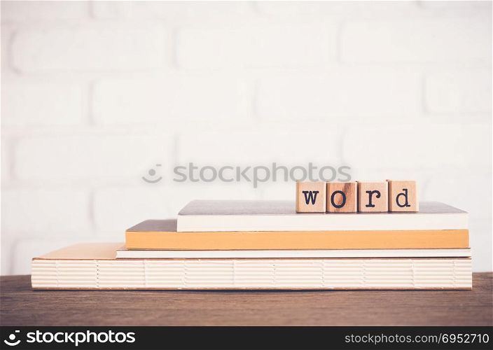 The Word letters, alphabet on wooden rubber stamps on top of books and table. White bricks background, blank copy space, vintage and minimal style. Language learning and education concepts.