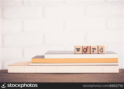 The Word letters, alphabet on wooden rubber stamps on top of books and table. White bricks background, blank copy space, vintage and minimal style. Language learning and education concepts.