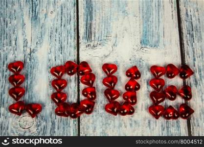 The word love arranged with red hearts on a wooden background in vintage style in bluish.Horizontal view.