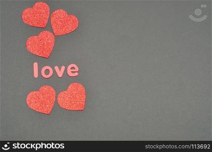 The word love on a black background decorated with five red glitter hearts