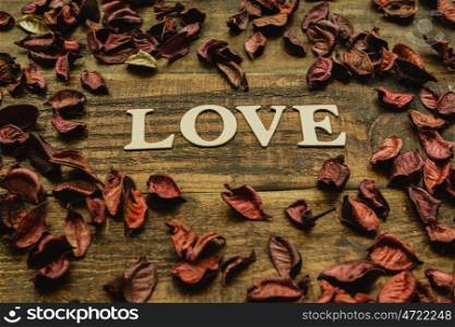 The word Love on a rustic wooden with dry red petals around