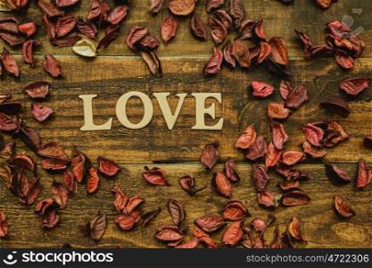 The word Love on a rustic wooden with dry red petals around