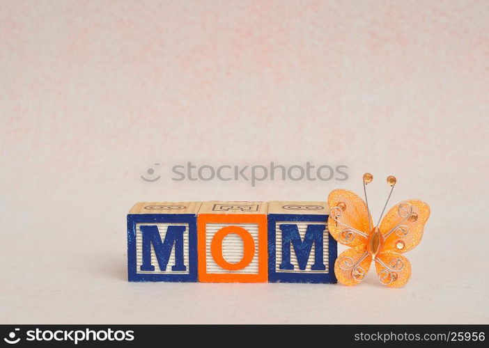 The word mom spelled with alphabet blocks against a white background and a silk butterfly