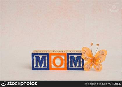 The word mom spelled with alphabet blocks against a white background and a silk butterfly