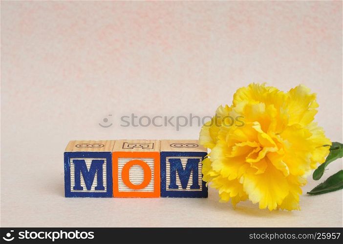 The word mom spelled with alphabet blocks against a white background with a yellow flower
