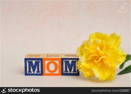 The word mom spelled with alphabet blocks against a white background with a yellow flower