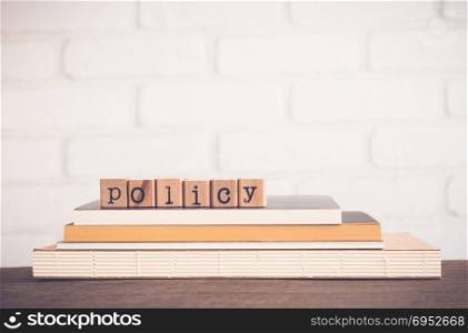 The word Policy, alphabet on wooden rubber stamps on top of books and table. Bricks background, blank copy space, vintage minimal style. Business privacy legal documents, advice information concepts.