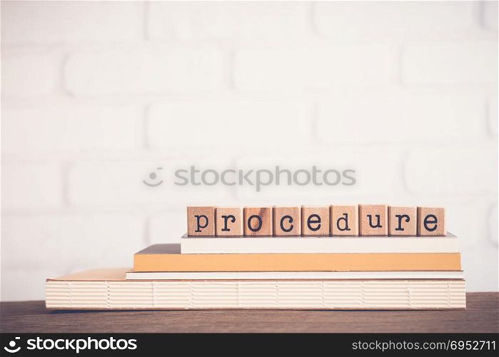 The word Procedure, alphabet on wooden rubber stamps on top of books and table. Bricks background, blank copy space, vintage minimal style. Business management, manual process, document information.