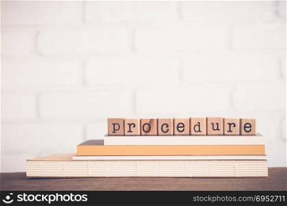 The word Procedure, alphabet on wooden rubber stamps on top of books and table. Bricks background, blank copy space, vintage minimal style. Business management, manual process, document information.