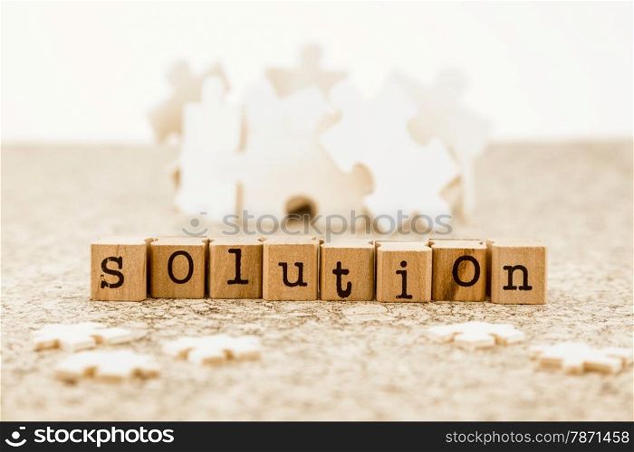 The word solution on wood stamps with little jigsaw pieces on foreground and group of large jigsaw pieces on background, idea of problem solving with brainstorm possible solutions