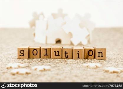 The word solution on wood stamps with little jigsaw pieces on foreground and group of large jigsaw pieces on background, idea of problem solving with brainstorm possible solutions