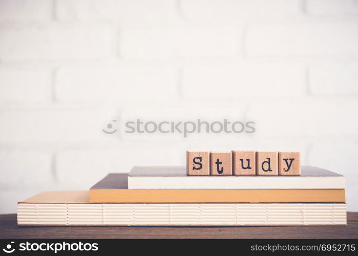 The word Study, alphabet on wooden rubber stamps on top of books and table. Bricks background, blank copy space, vintage minimal style. Knowledge, learning, training course and education concepts.