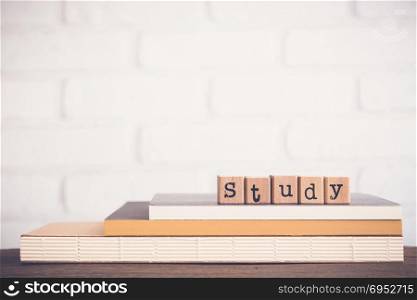 The word Study, alphabet on wooden rubber stamps on top of books and table. Bricks background, blank copy space, vintage minimal style. Knowledge, learning, training course and education concepts.