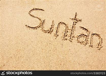 The word suntan written in the sand on a beach