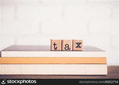 The word Tax, alphabet on wooden rubber stamps on top of books and table. Bricks background, blank copy space, vintage minimal style. Financial, accounting, income and business management concepts