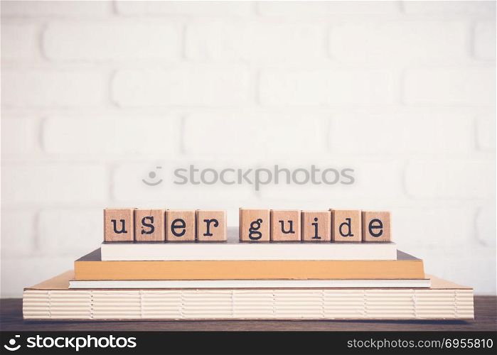 The word User guide, text on wooden cubes on top of books. Background copy space, vintage minimal. Concepts of manual or technical communication document to give assistance about using system.