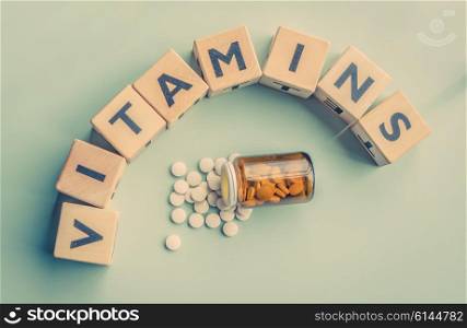 The word vitamins on a table with a glass of pills