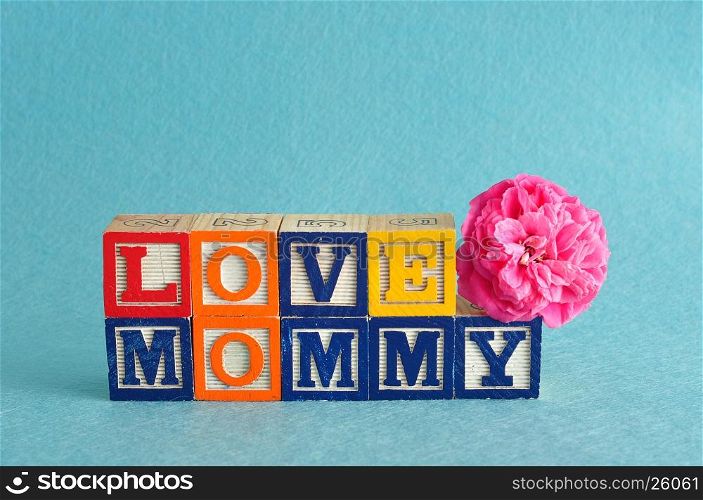The words love mommy spelled with alphabet blocks against a blue background with a pink flower