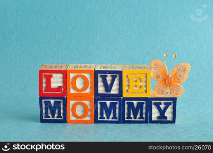 The words love mommy spelled with alphabet blocks against a blue background with a orange butterfly