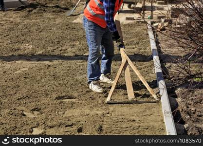 The worker aligns the basement with a wooden level to start laying paving slabs on the working pedestrian zone.. The worker aligns the foundation with a wooden level for laying tiles on the sidewalk.