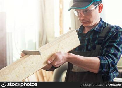 The worker makes measurements of a wooden board with corner ruler. Profession, carpentry and woodwork concept.. The worker makes measurements of a wooden board