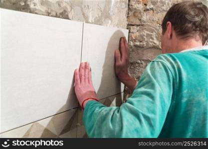 The worker puts tiles on the wall. Finishing works, blurred focus. The technology of laying tile.. Repair and finishing works