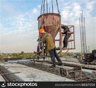The workers on a building infrastructure roof with machinery and tools. Pouring concrete into a mold. Workers on a building infrastructure roof with machinery and tools