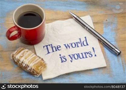 The world is yours - a positive affirmation. Handwriting on a napkin with a pen, cup of espresso coffee and cookie against grunge painted wood