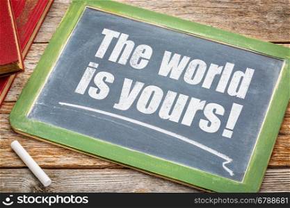 The world is yours - a positive affirmation. White chalk text on a blackboard with books.