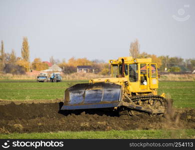 The yellow tractor with attached grederom makes ground leveling. Work on the drainage system in the field.. The yellow tractor with attached grederom makes ground leveling.