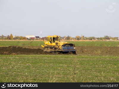 The yellow tractor with attached grederom makes ground leveling. Work on the drainage system in the field.. The yellow tractor with attached grederom makes ground leveling.