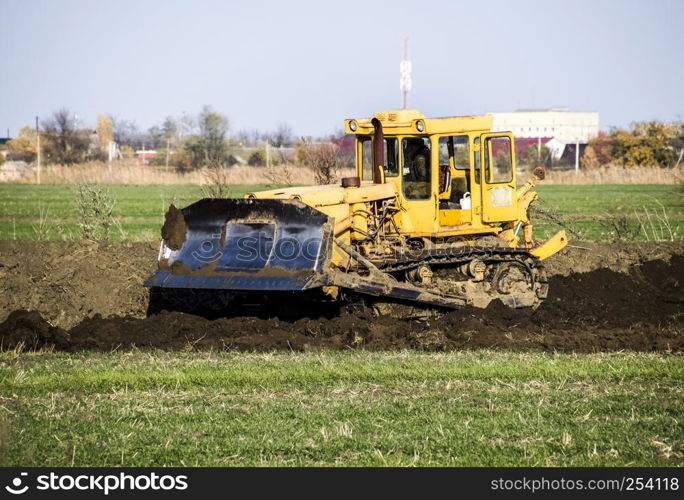 The yellow tractor with attached grederom makes ground leveling. Work on the drainage system in the field.. The yellow tractor with attached grederom makes ground leveling.