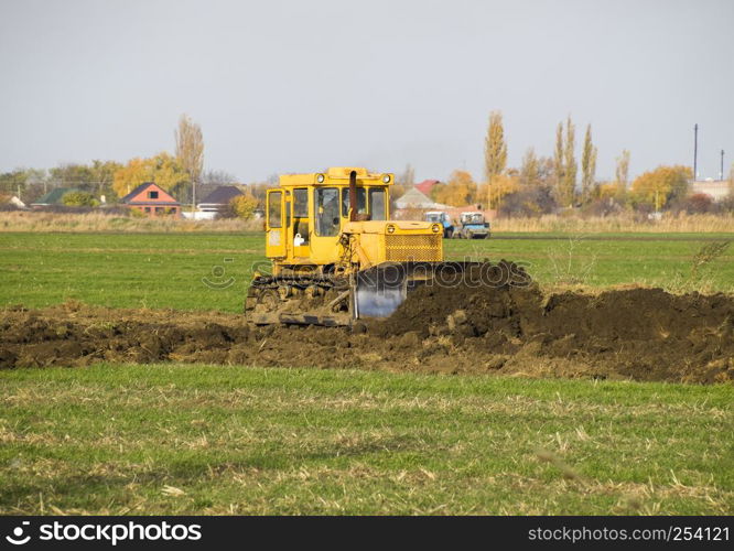 The yellow tractor with attached grederom makes ground leveling. Work on the drainage system in the field.. The yellow tractor with attached grederom makes ground leveling.