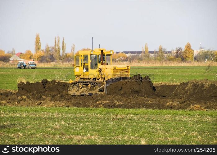 The yellow tractor with attached grederom makes ground leveling. Work on the drainage system in the field.. The yellow tractor with attached grederom makes ground leveling.