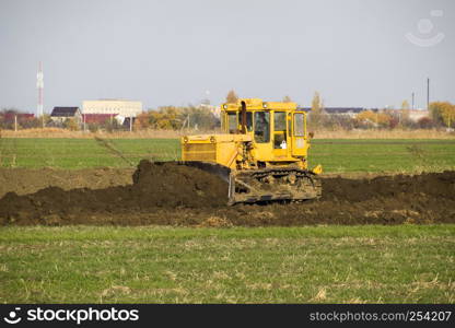 The yellow tractor with attached grederom makes ground leveling. Work on the drainage system in the field.. The yellow tractor with attached grederom makes ground leveling.
